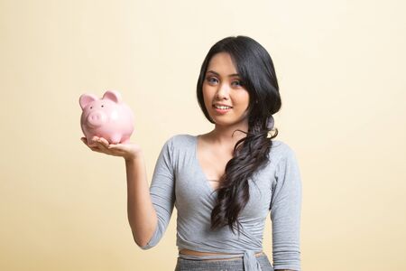 Young Asian woman with a pig coin bank   on beige backgroundの写真素材