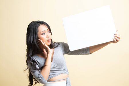 Young Asian woman  surprise with  white blank sign   on beige backgroundの写真素材