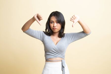 Unhappy Asian girl show thumbs down with both hands   on beige backgroundの写真素材