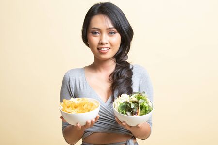 Young Asian woman with potato chips and salad   on beige backgroundの写真素材