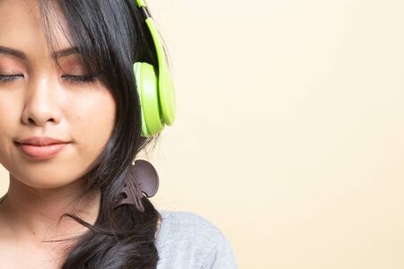Pretty asian girl listening music with her headphones   on beige backgroundの写真素材