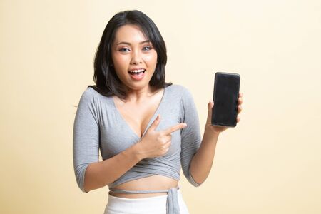 Excited Young Asian woman point to mobile phone   on beige backgroundの写真素材