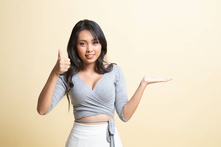 Beautiful young Asian woman show palm hand and thumbs up   on beige backgroundの写真素材