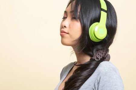 Pretty asian girl listening music with her headphones   on beige backgroundの写真素材