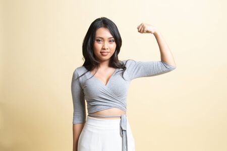 Beautiful young Asian woman flex bicep   on beige backgroundの写真素材