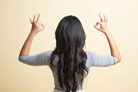 Back view of Asian woman show double OK hand sign   on beige backgroundの写真素材