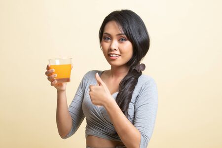 Young Asian woman thumbs up drink orange juice   on beige backgroundの写真素材