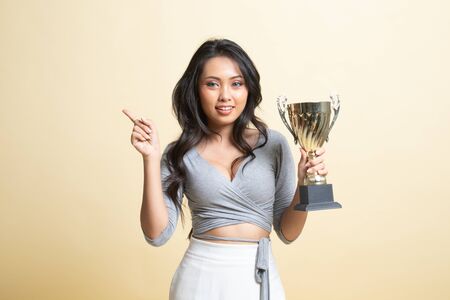 Successful young asian woman holding a trophy point to blank space   on beige backgroundの写真素材