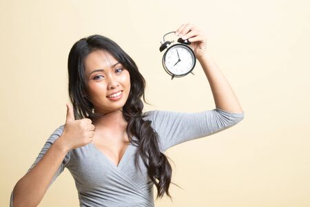 Young Asian woman show thumbs up with a clock   on beige backgroundの写真素材