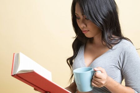 Young Asian woman with a book and cup of coffee   on beige backgroundの写真素材