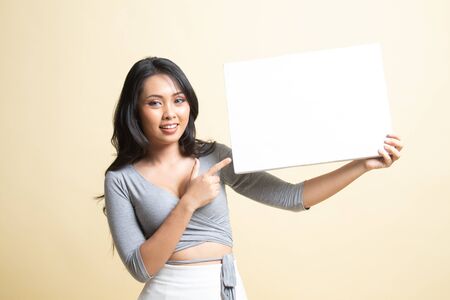 Young Asian woman point to  blank sign   on beige backgroundの写真素材
