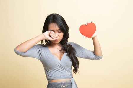 Asian woman sad and cry with red heart   on beige backgroundの写真素材