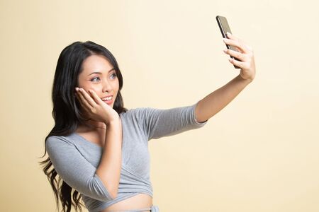 Young Asian woman selfie with mobile phone   on beige backgroundの写真素材