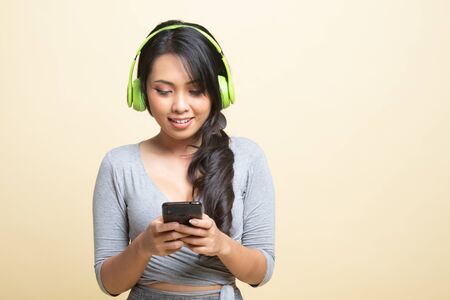 Pretty asian girl listening music with her headphones   on beige backgroundの写真素材
