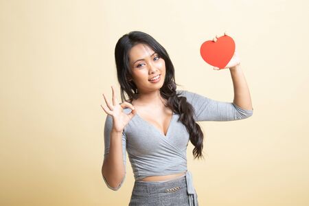 Asian woman show OK with red heart   on beige backgroundの写真素材