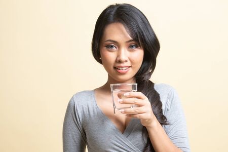 Young Asian woman with a glass of drinking water   on beige backgroundの写真素材