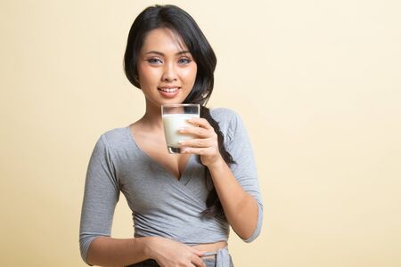 Healthy Asian woman drinking a glass of milk   on beige backgroundの写真素材