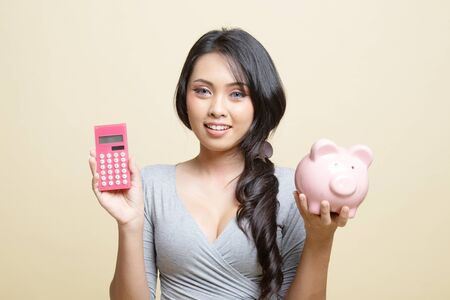 Asian woman with calculator and piggy bank   on beige backgroundの写真素材