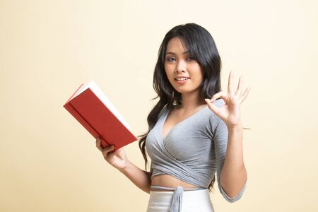 Young Asian woman show OK with a book   on beige backgroundの写真素材