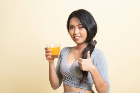Young Asian woman thumbs up drink orange juice   on beige backgroundの写真素材