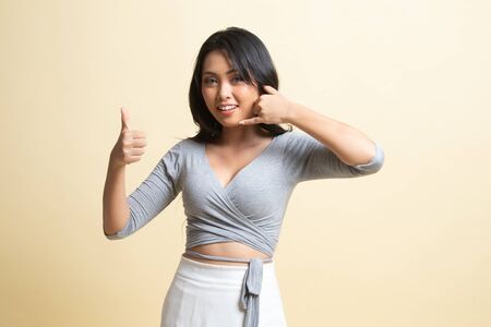 Young Asian woman thumbs up show with phone gesture   on beige backgroundの写真素材