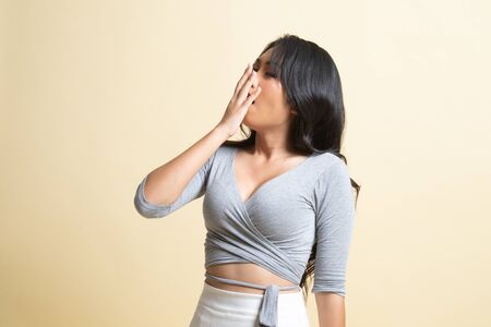 Sleepy young Asian woman yawn   on beige backgroundの写真素材