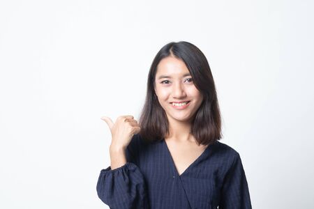 Young Asian woman smile and point to copy space with her thumb on white backgroundの写真素材