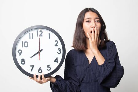 Sleepy young Asian woman with a clock in the morning on white backgroundの写真素材