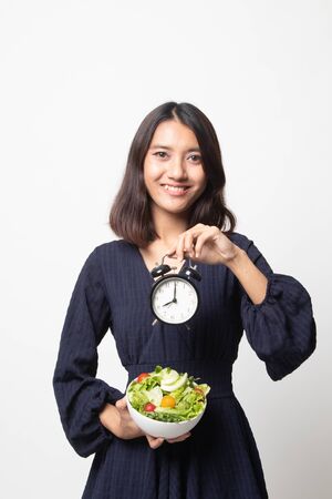 Young Asian woman with clock and salad on white backgroundの写真素材