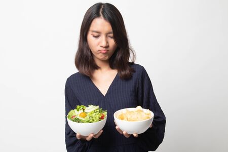 Young Asian woman with potato chips and salad on white backgroundの写真素材