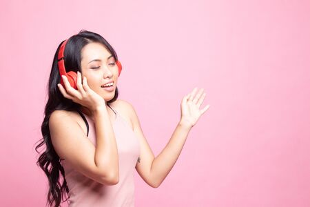 Pretty asian girl listening music with her headphones on pink backgroundの写真素材