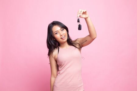 Cute asian girl showing car  key on pink backgroundの写真素材