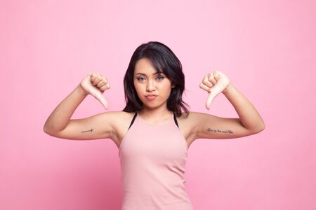 Unhappy Asian girl show thumbs down with both hands on pink backgroundの写真素材