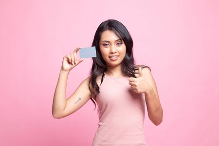 Young Asian woman thumbs up with a blank card on pink backgroundの写真素材