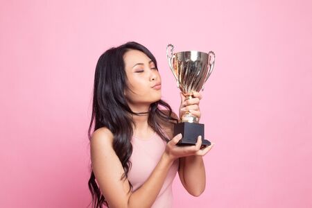 Successful young asian woman holding kissing a trophy on pink backgroundの写真素材