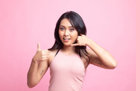 Young Asian woman thumbs up show with phone gesture on pink backgroundの写真素材