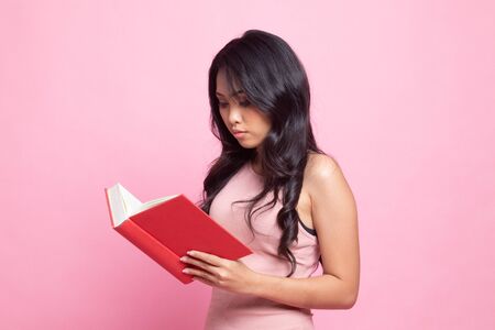Young Asian woman read a book on pink backgroundの写真素材
