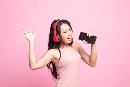 Pretty asian girl listening music with her headphones on pink backgroundの写真素材