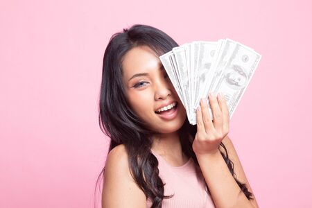 Portrait of  young asian woman  showing bunch of money banknotes on pink backgroundの写真素材