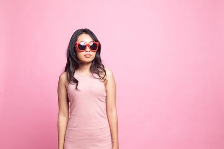 Portrait of a beautiful young asian girl in sunglasses on pink backgroundの写真素材