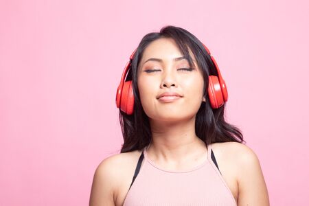 Pretty asian girl listening music with her headphones on pink backgroundの写真素材