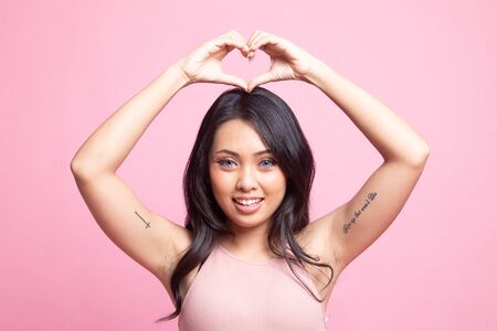 Young Asian woman gesturing heart hand sign on pink backgroundの写真素材