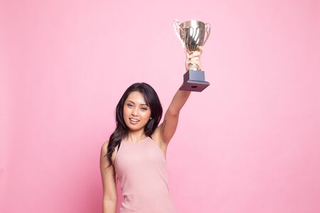 Successful young asian woman holding a trophy on pink backgroundの写真素材