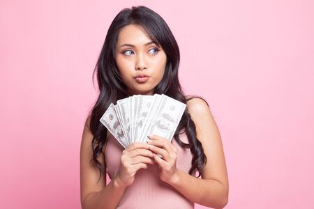 Portrait of  young asian woman  showing bunch of money banknotes on pink backgroundの写真素材