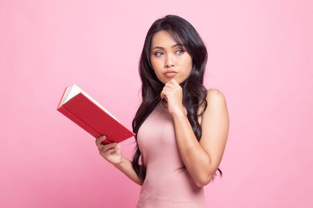 Young Asian woman with a book is thinking on pink backgroundの写真素材