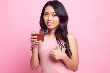 Young Asian woman thumbs up with tomato juice on pink backgroundの写真素材