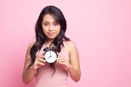 Young Asian woman smile with a clock on pink backgroundの写真素材