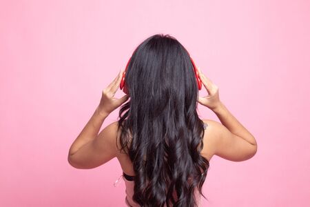 Pretty asian girl listening music with her headphones on pink backgroundの写真素材
