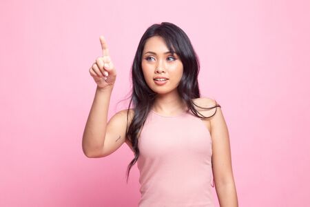 Asian woman touching the screen with her finger on pink backgroundの写真素材