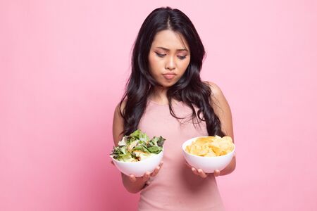 Young Asian woman with potato chips and salad on pink backgroundの写真素材